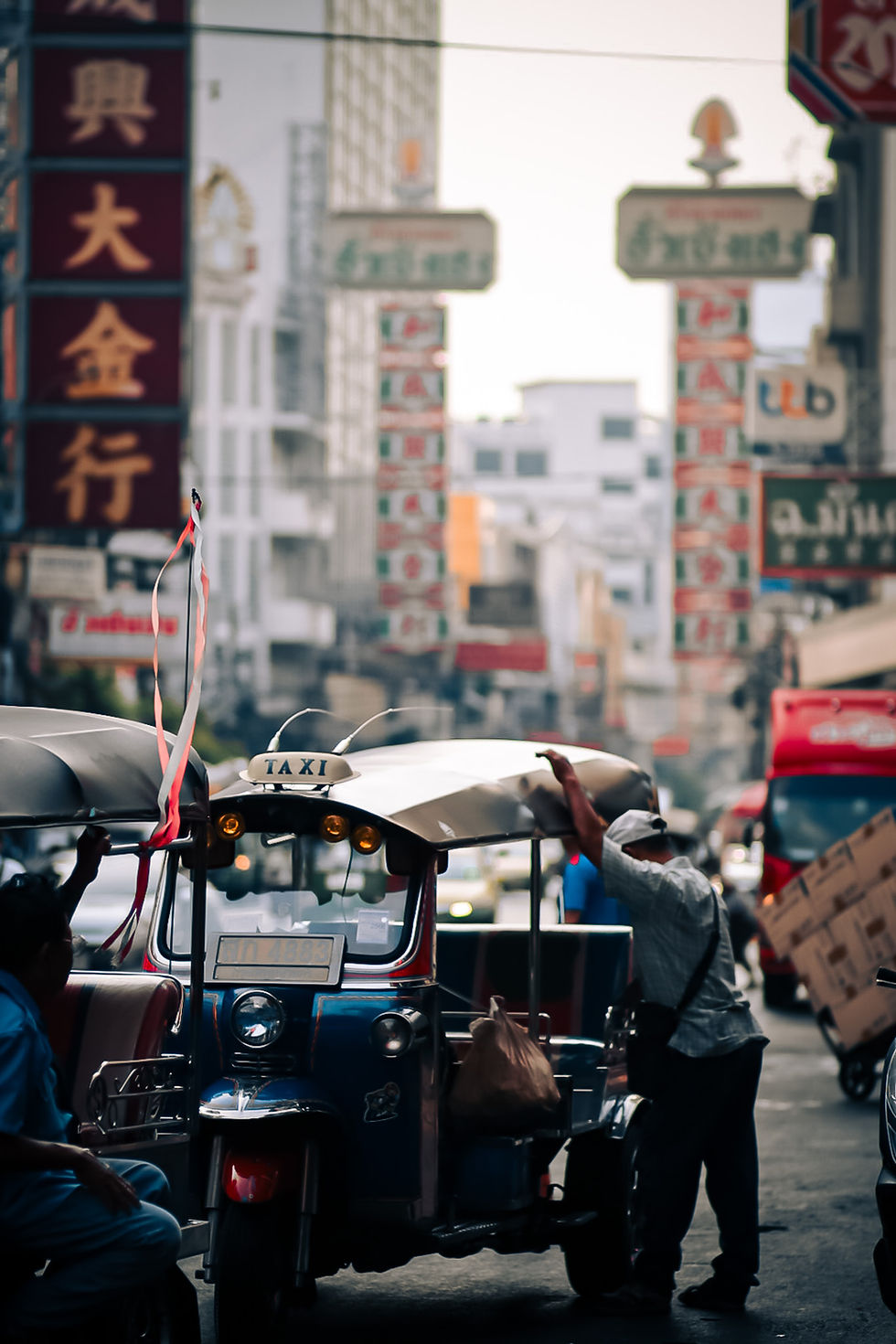 Tuk-tuk driver unloading supplies in crowded street of Chinatown Bangkok