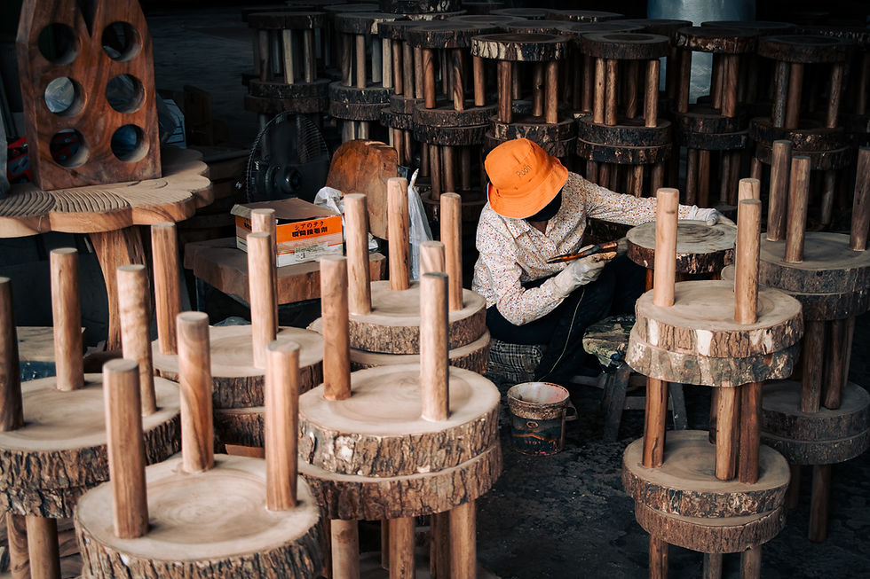 Thai woman in orange hat assembling rustic wooden stools in a Chiang Mai furniture workshop.