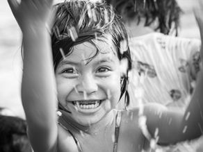 Laughing girl playing with water, captured mid-motion in black and white.