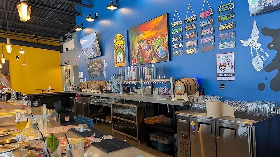 Modern bar interior with blue and yellow walls, beer taps, glasses, and artwork. Menu and glasses on counter; hanging lights above.