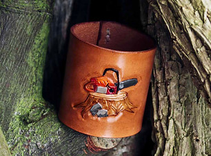 Nestle in a stack of wood is a brown napkin ring 5cm high and round with a carved and painted chainsaw on the front