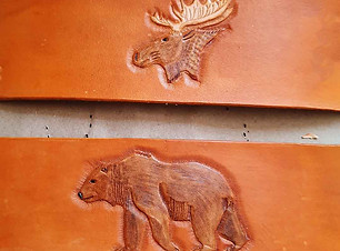 Two brown napkin rings that that are flat before sewn. Top ring features a brown moose head and the bottom ring features a walking brown bear.