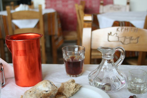 Red jug, glass, and water pitcher on table with chairs in background.
