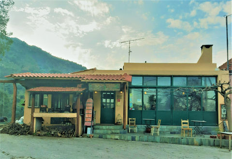 Rustic restaurant exterior with green door and windows, mountain backdrop, and cloudy sky.