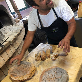 Chef near a brick oven with freshly baked bread, smiling, looking up.