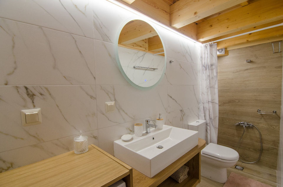 Bathroom with a toilet, sink, shower, and a round mirror.