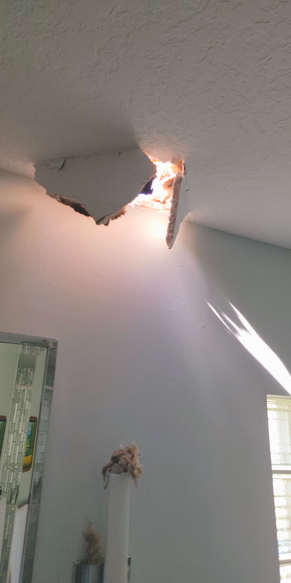 Damaged ceiling with a large hole and torn drywall letting daylight into a white room, suggesting urgent repair needed