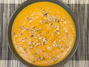 Bol de velouté de patate douce au curry vegan, une recette saine, originale et de saison, décoré de noisettes et de coco râpée.