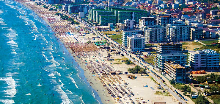 Plajă aglomerată cu șezlonguri și umbreluțe, valuri albastre, clădiri înalte în fundal, o zi însorită de vară, atmosferă vibrantă.