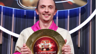 Bărbat zâmbitor ținând un trofeu rotund cu inscripția "Chef Claudiu Gherguț 30.000€". Fundal cu lumini și cercuri. Emoție de triumf.