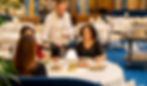 Chelner servește vin unui grup de persoane într-un restaurant elegant, cu decor albastru și auriu. Atmosferă rafinată.