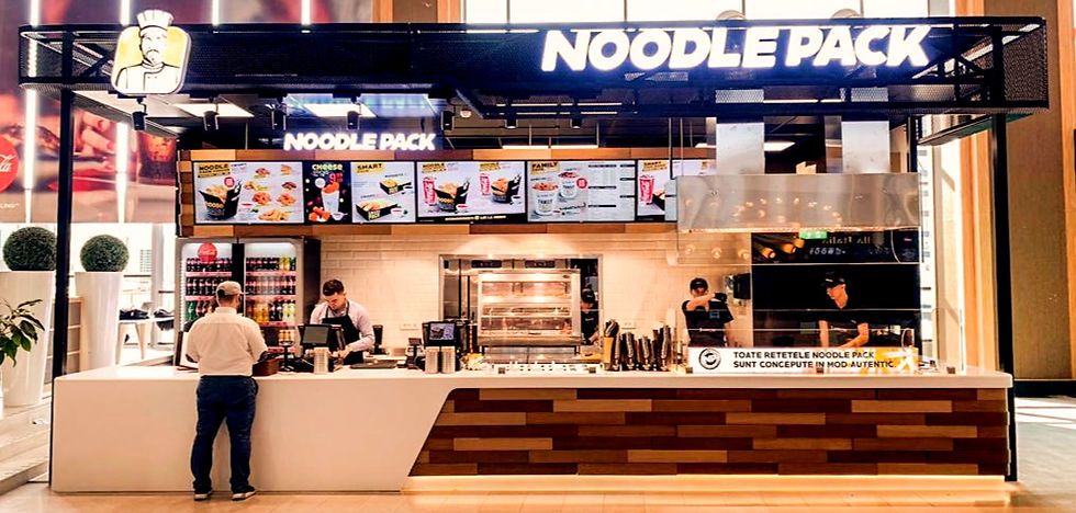 Bărbat așteaptă la standul de mâncare Noodle Pack în mall. Două persoane prepară comenzi. Fundal cu panouri luminoase și meniu colorat.