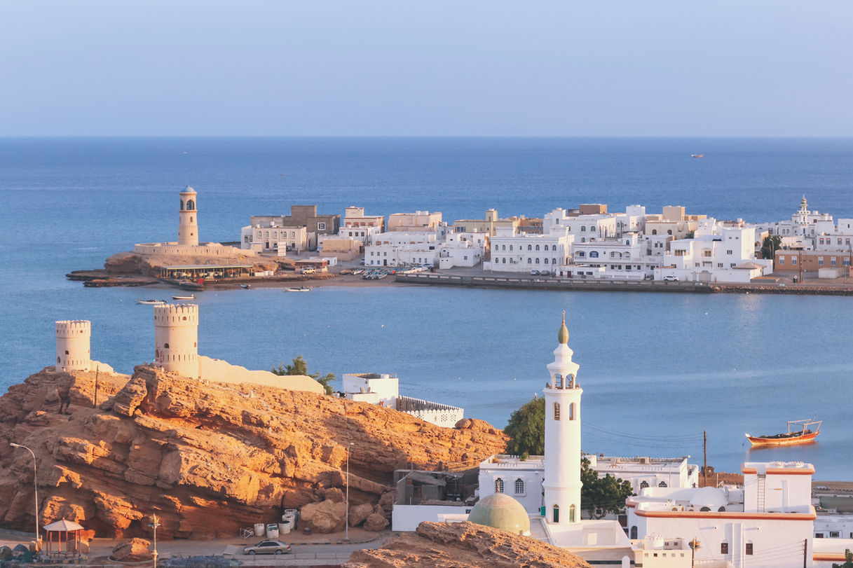 Coastal town with white buildings, mosque, and watchtower by blue sea.