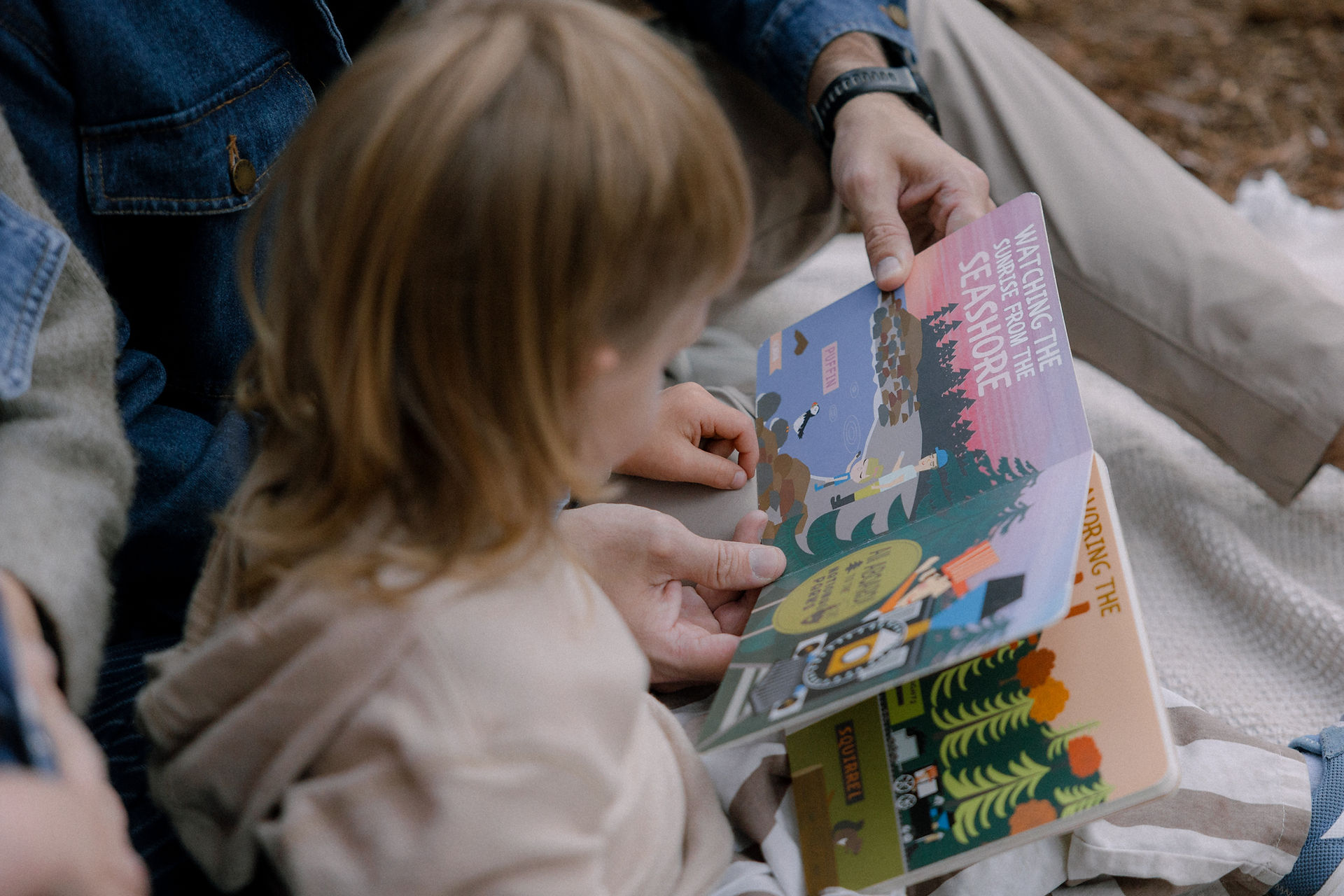 A family of four sits on a blanket and reads All Aboard National Parks by Haily Meyers