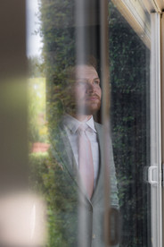 groom's reflection in a window as he stands with his hands in his pockets