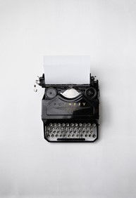 Picture of a black typewriter with silver keys and a blank piece of paper sitting in it taken from above. The background is completely white.