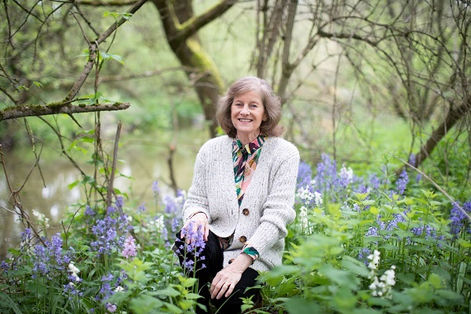 Smiling woman sitting amongst bluebells with river in the background