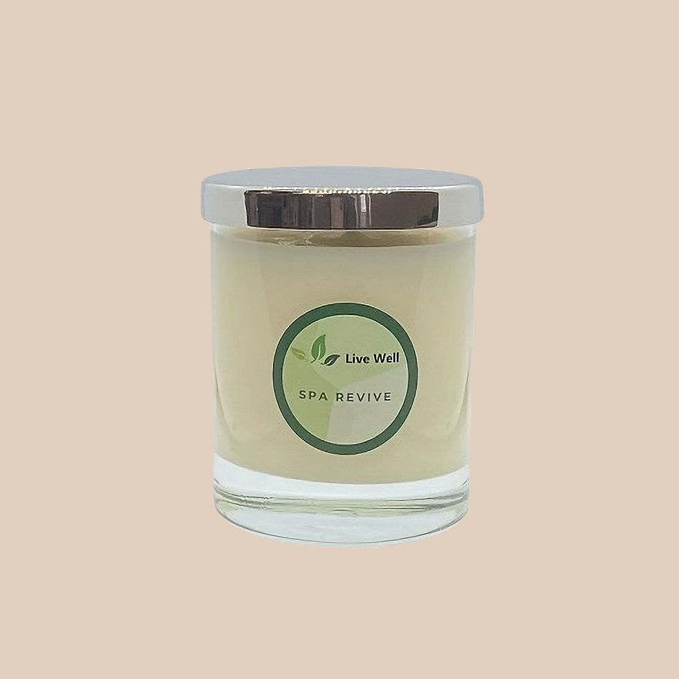 White candle in a glass jar with silver lid on tan background. Green label reads "Live Well, SPA REVIVE." Calm, soothing ambiance.