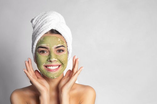 Smiling person with green tea 
 face mask and towel on head.