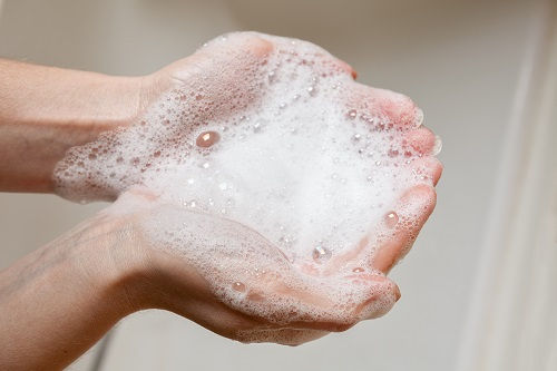 Hands cupped with white soap lather, against a neutral background. The image conveys cleanliness and hygiene.