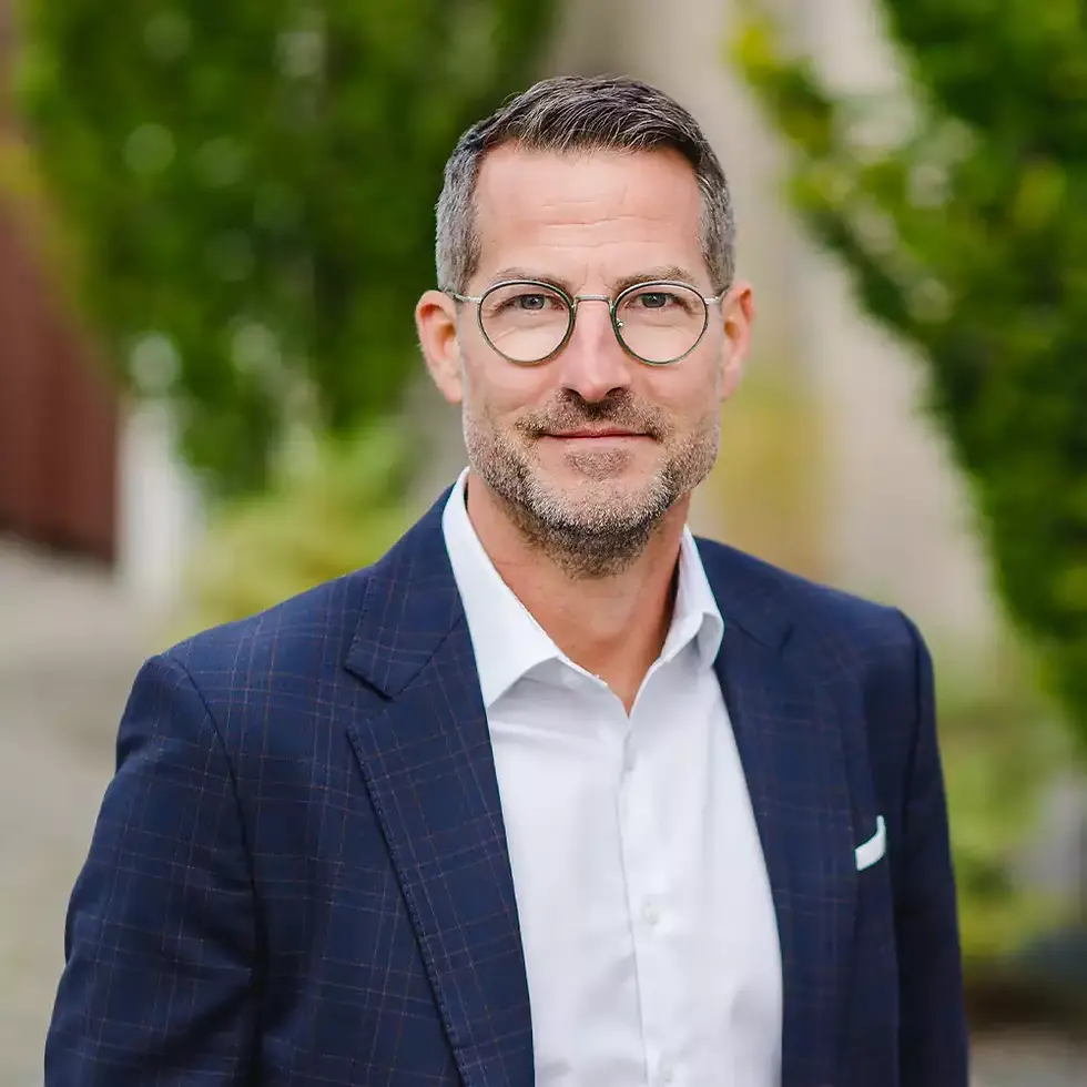 Mann mit Brilleund Anzug lächelt fontal in Kamera