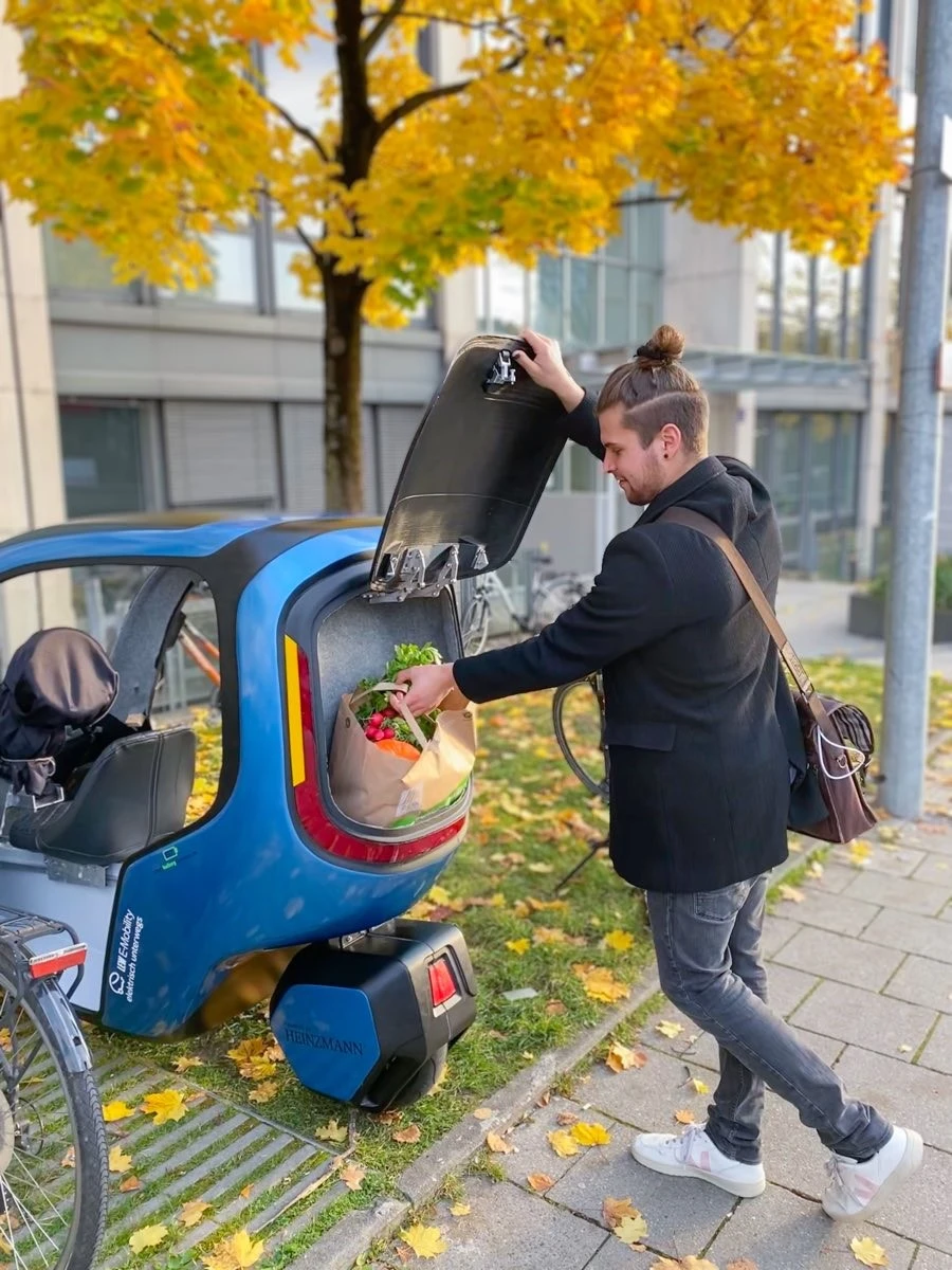 Mann belädt den kleinen Kofferraum eines blauen Mini-Fahrzeugs
