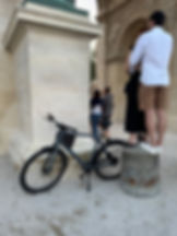 graues Bike parkt an historischen Tor, dabei steht ein Pärchen auf Sockel daneben.