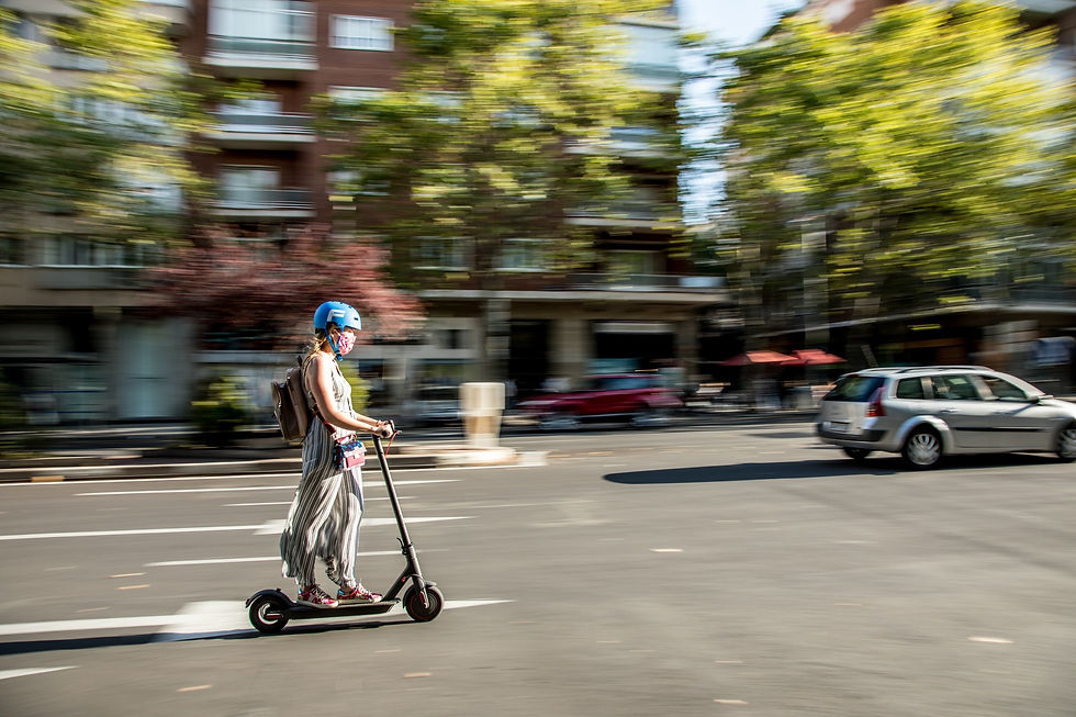 Frau mit Helm fährt mit e-Scooter auf Straße.