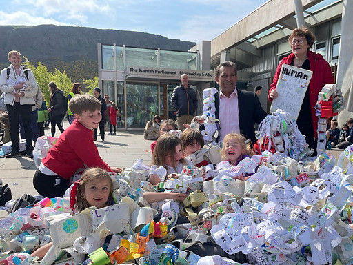 Young children under a sea of paper chains, sitting outside a building, with some older people smiling next to them.