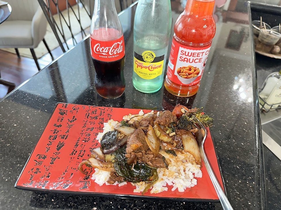 Plate of rice topped with stir-fried beef and vegetables on a red Chinese-character plate, with Coke, Topo Chico, and sweet chili sauce bottles nearby