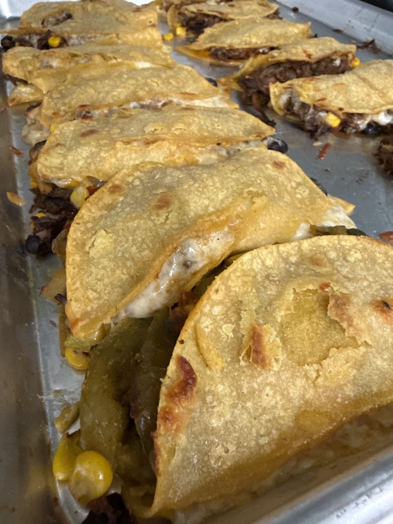 Tray of baked beef tacos with melted cheese and corn, arranged in a metal pan, warm and appetizing.