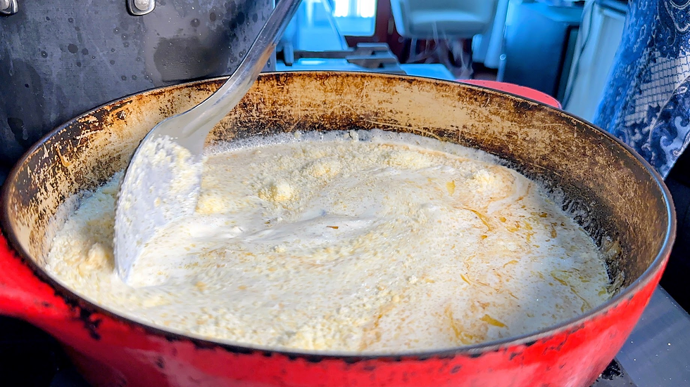 Creamy sauce simmering in a red pot, stirred with a ladle in a busy kitchen.