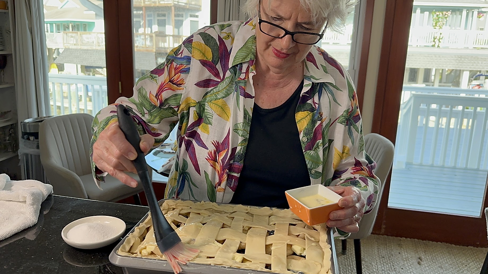 Woman in glasses brushes egg wash on a lattice pie crust in a bright home kitchen, focused and intent.