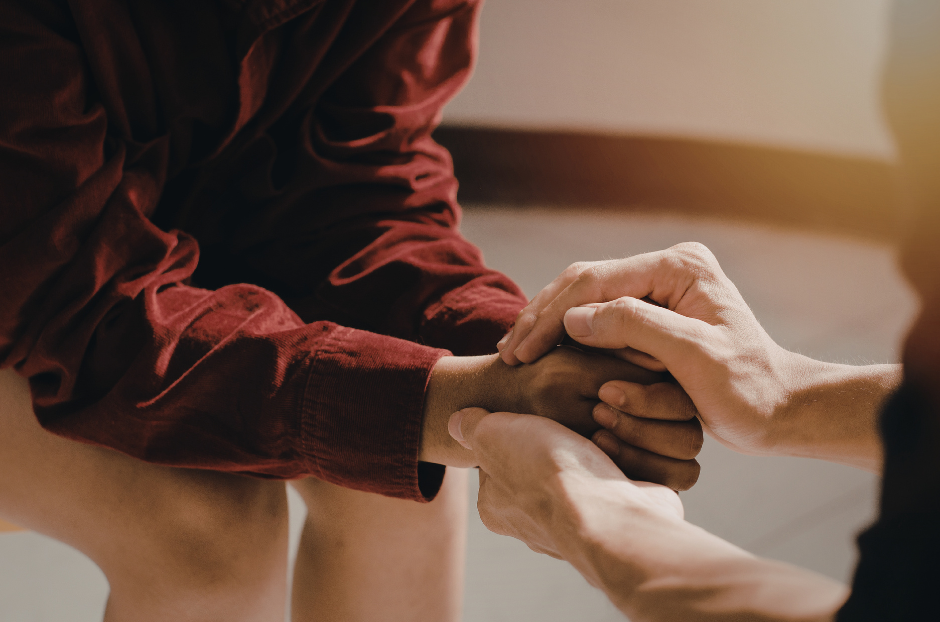Two people of different ethnicities holding hands in support, love, and care.