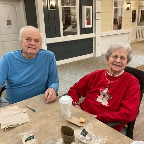 Barbara Wagner and Fr. John Ossola sitting at a table at their memory care facility.