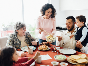 Family around a breakfast table mother, grandmother, father, adolescent daughter, and toddler son smiling and passing food