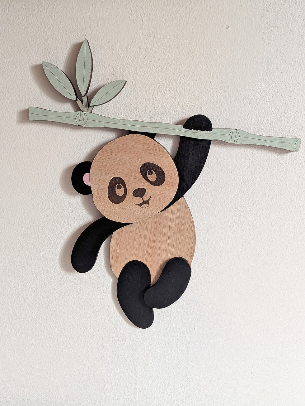 Panda en bois suspendu à sa branche de bambou présenté avec une peluche panda, décoration chambre bébé.