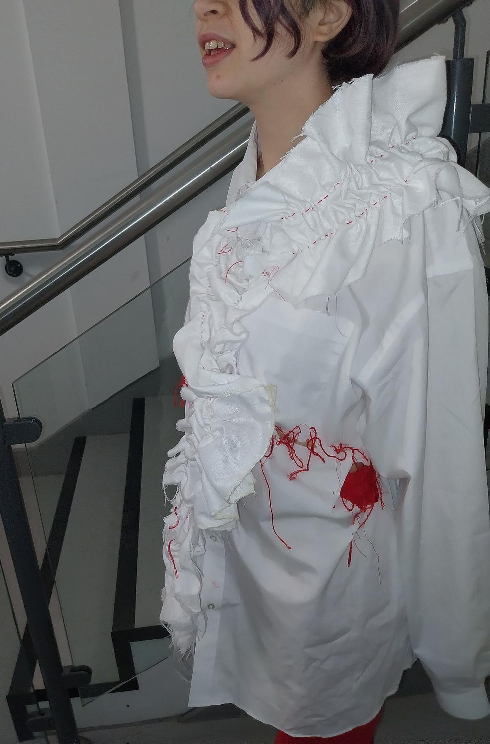 Person wearing embroidered white shirt with ruffles and red embroidered text reading "my gender is not debatable"