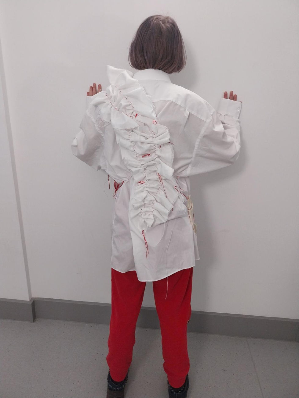 Person wearing embroidered white shirt with ruffles and red embroidered text reading "my gender is not debatable"