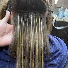 Woman's hair showing individual blonde extensions during professional installation process.
