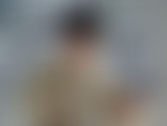 Man in a beige coat drinks from a white mug while checking his watch. Black-and-white photos on the gray wall create a focused mood.