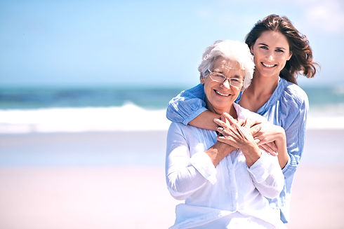 Portrait, beach and young woman with her senior mother embrace and smile together outdoors