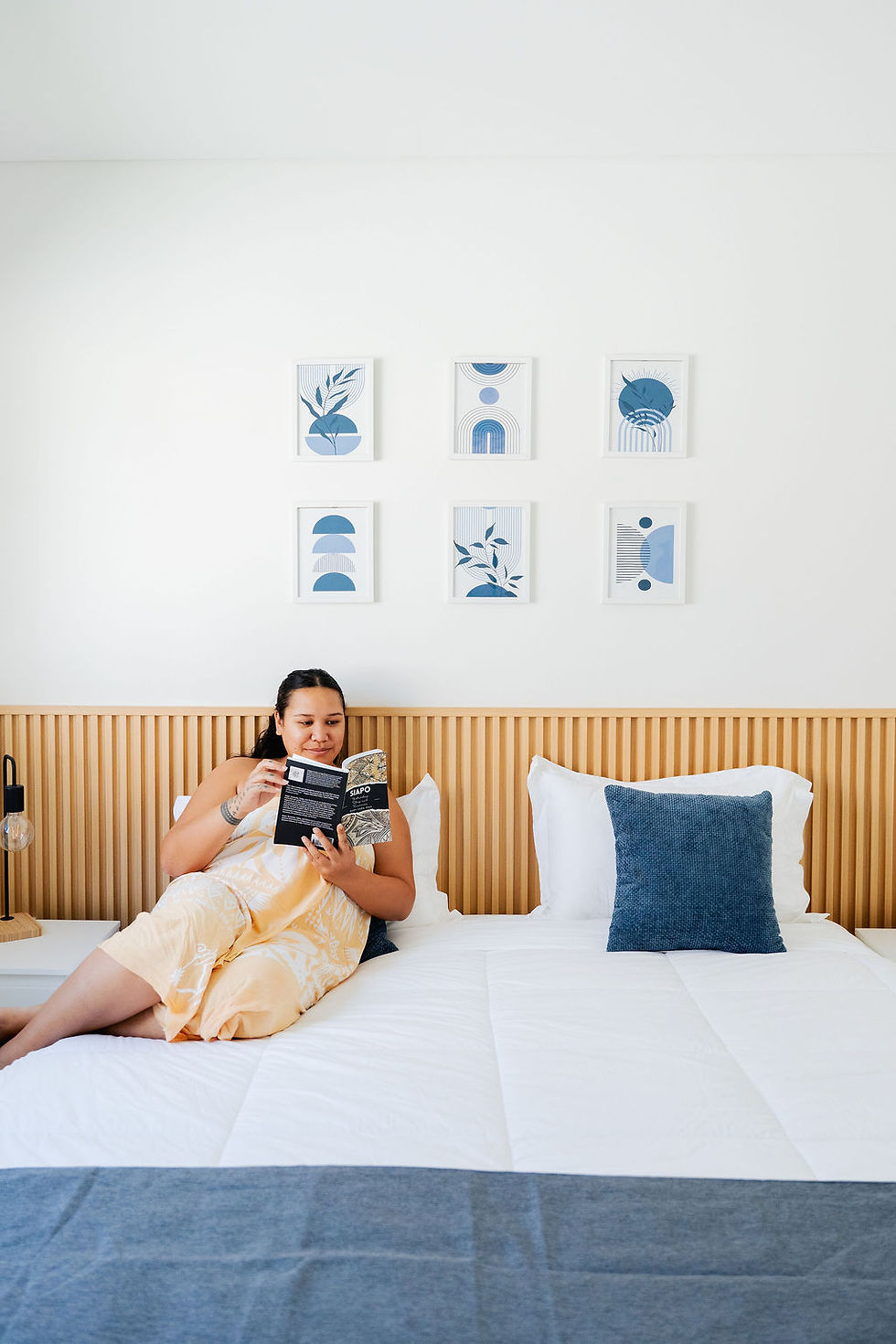 Woman reading a book in a bright hotel room bed.