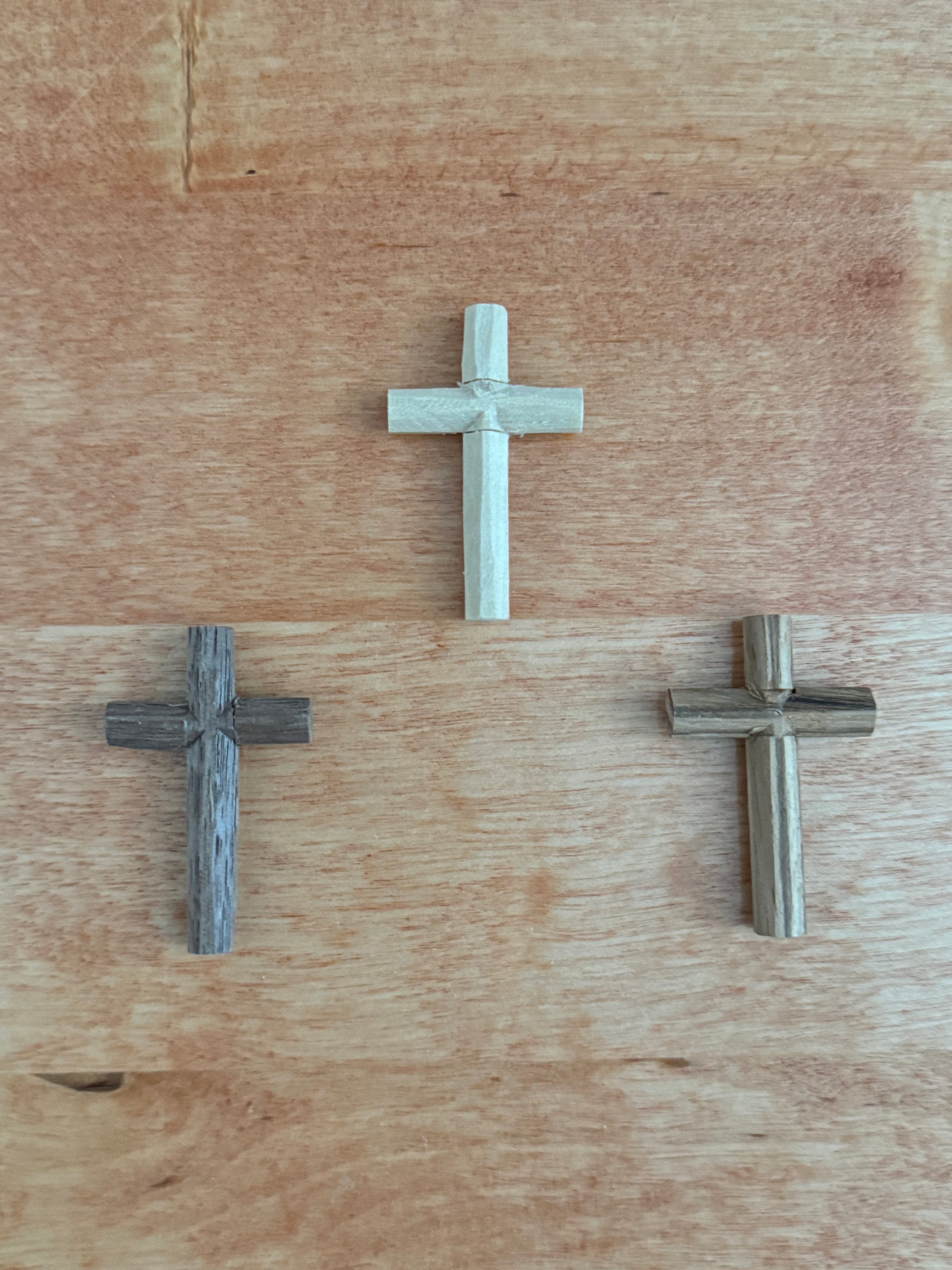 Three rustic wood cross necklaces on a wooden surface