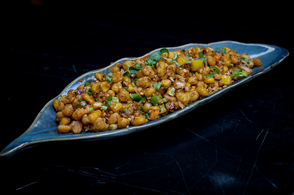 Spiced corn and vegetables garnished with herbs, served on a blue leaf-shaped platter against a black background.
