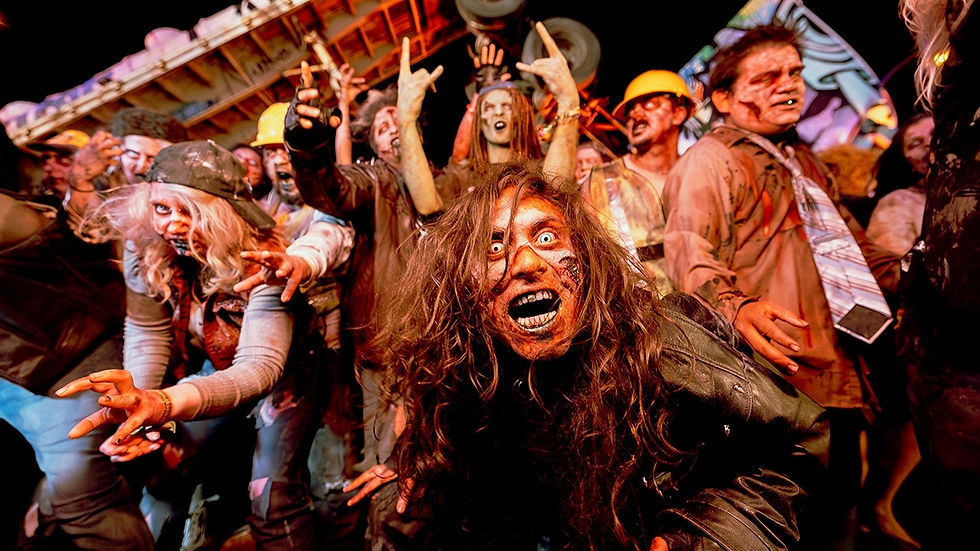 A crowd of people in zombie costumes and makeup pose at a spooky nighttime horror event.