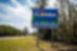 Welcome to Florida sign by a rural road, featuring blue sky and trees. Text: "FLORIDA, THE SUNSHINE STATE, Governor Ron DeSantis."
