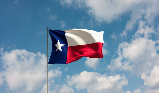 Texas flag waving against a blue sky with clouds, featuring blue, white, and red stripes and a white star, evoking a sense of pride.