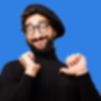 Smiling artsy man wearing a beret connecting with his inner artist and pointing to himself with a blue background.