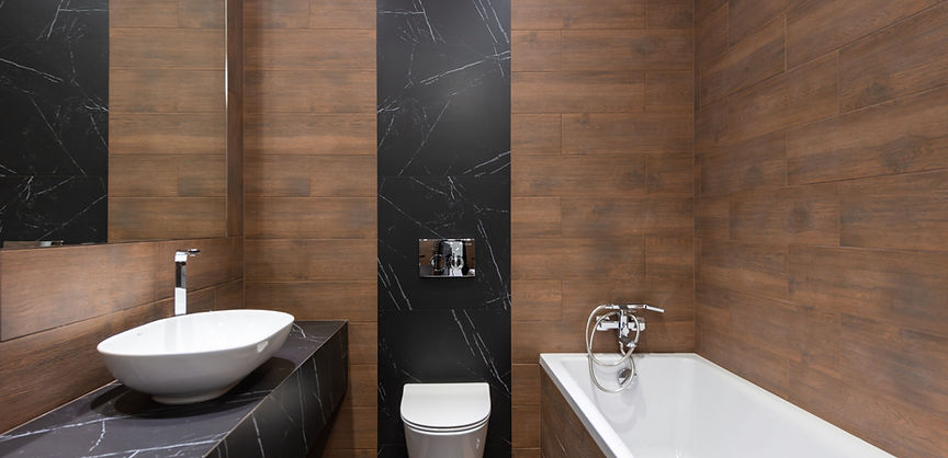 Wood-look tiled bathroom with white bath, vessel basin and black marble accents